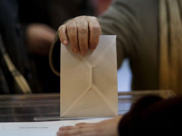Una persona introduce un sobre en una urna electoral. Una persona introduce un sobre en una urna electoral.