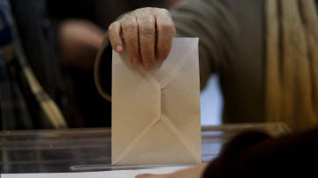 Una persona introduce un sobre en una urna electoral.