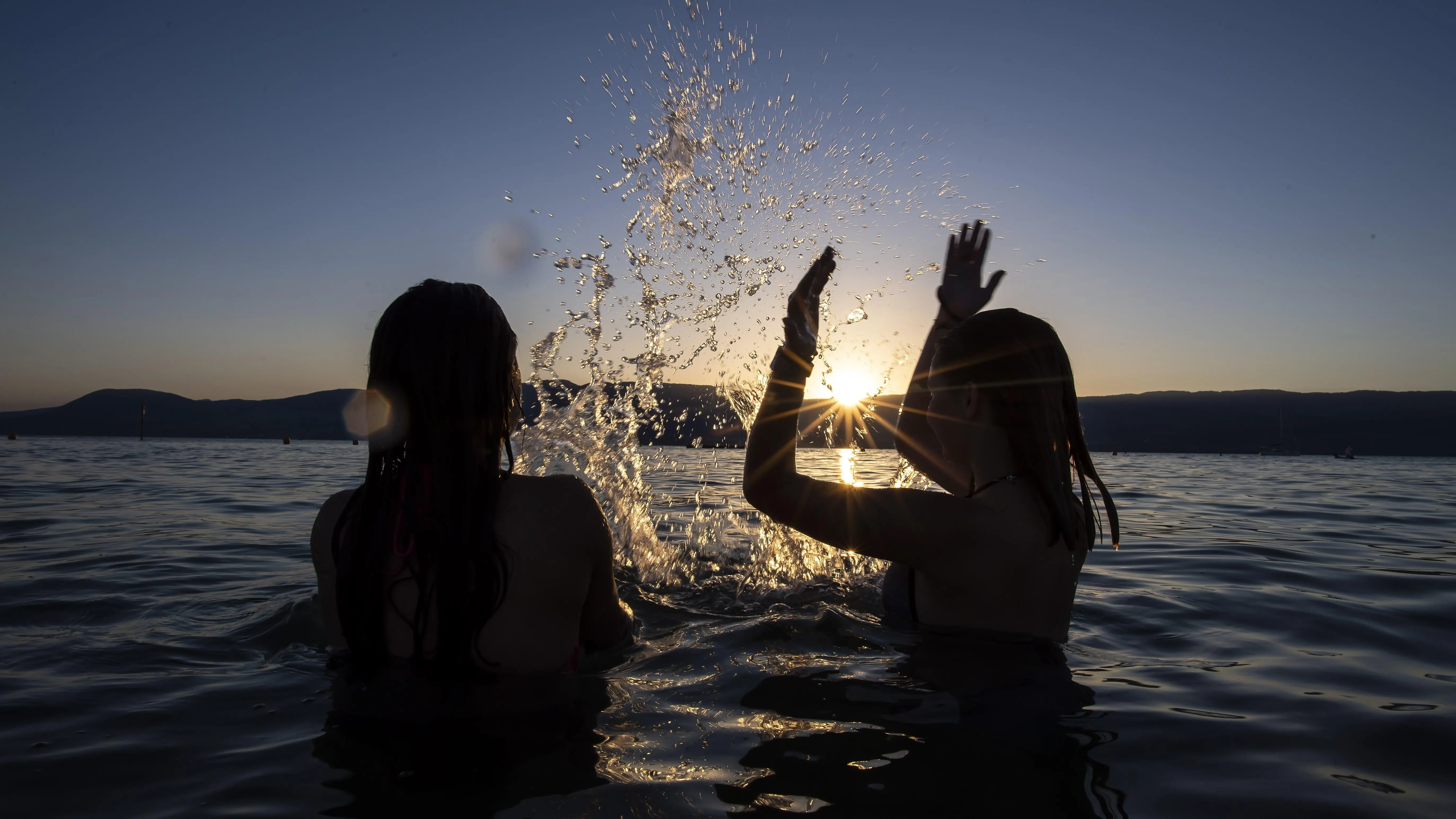 Dos adolescentes disfrutan de la puesta de sol en el agua del Lago de Neuchatel