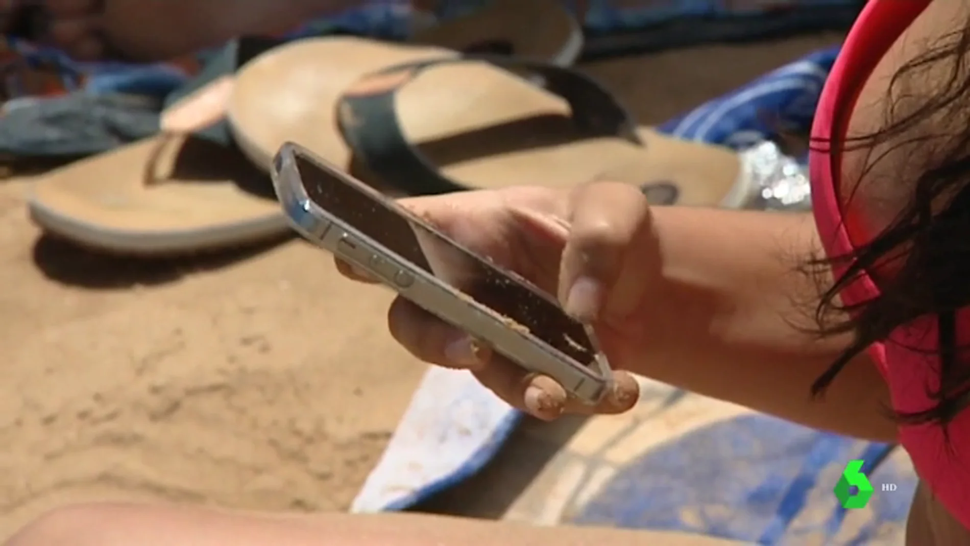 Una persona con un teléfono móvil en la playa. 