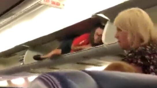 Una azafata se mete en el compartimento de las maletas del avi&oacute;n para saludar a los pasajeros