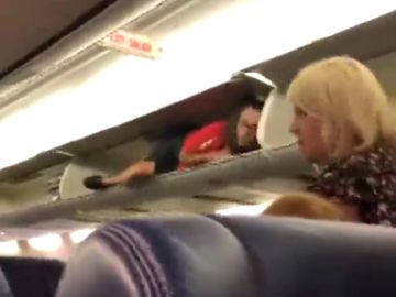 Una azafata se mete en el compartimento de las maletas del avión para saludar a los pasajeros Una azafata se mete en el compartimento de las maletas del avión para saludar a los pasajeros
