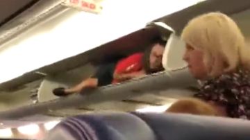 Una azafata se mete en el compartimento de las maletas del avión para saludar a los pasajeros