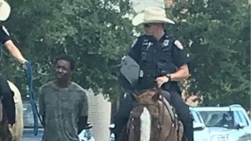 Dos policías transportan a un hombre negro atado con una cuerda.