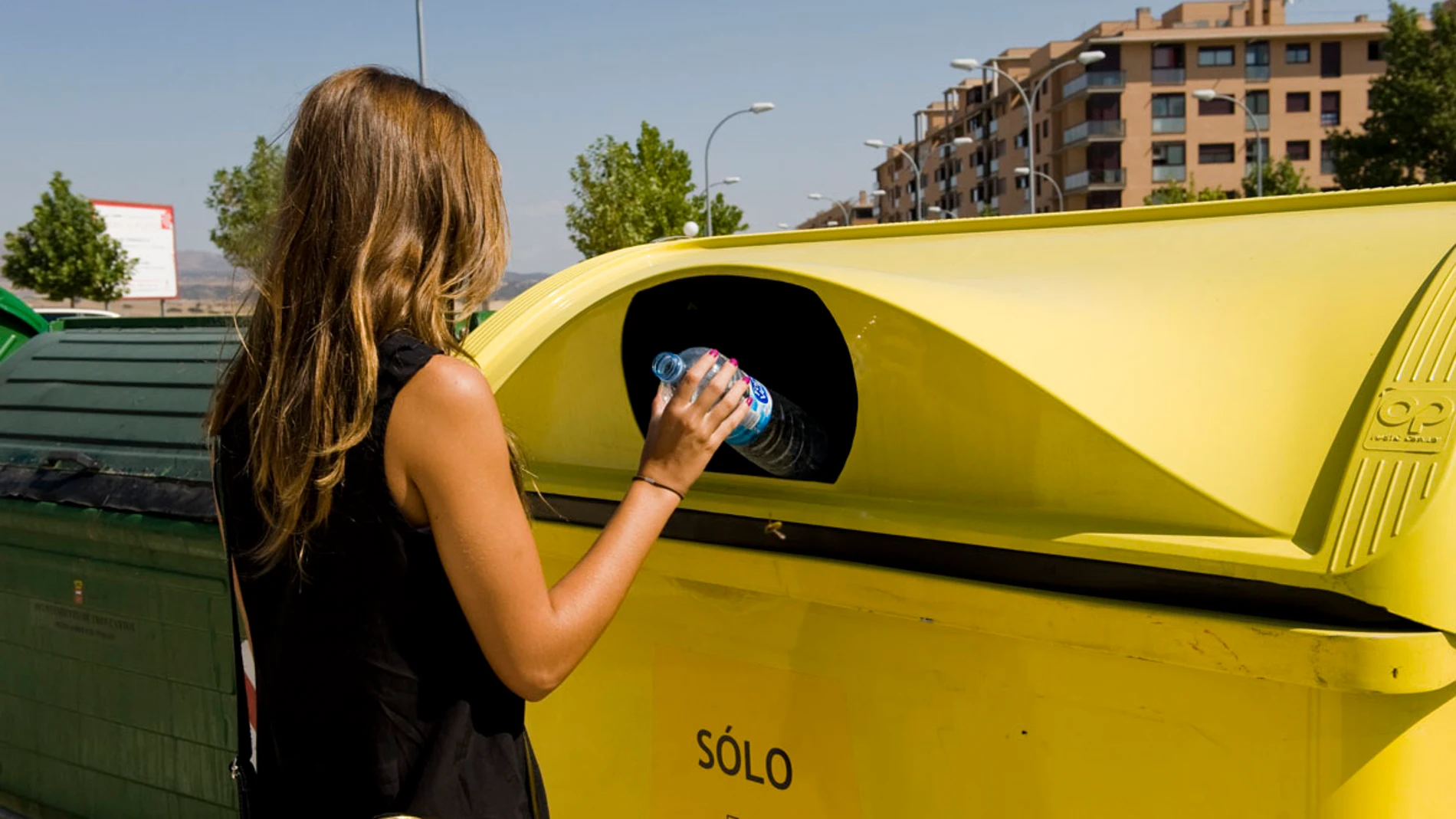 Una mujer tira una botella en el contenedor amarillo. 
