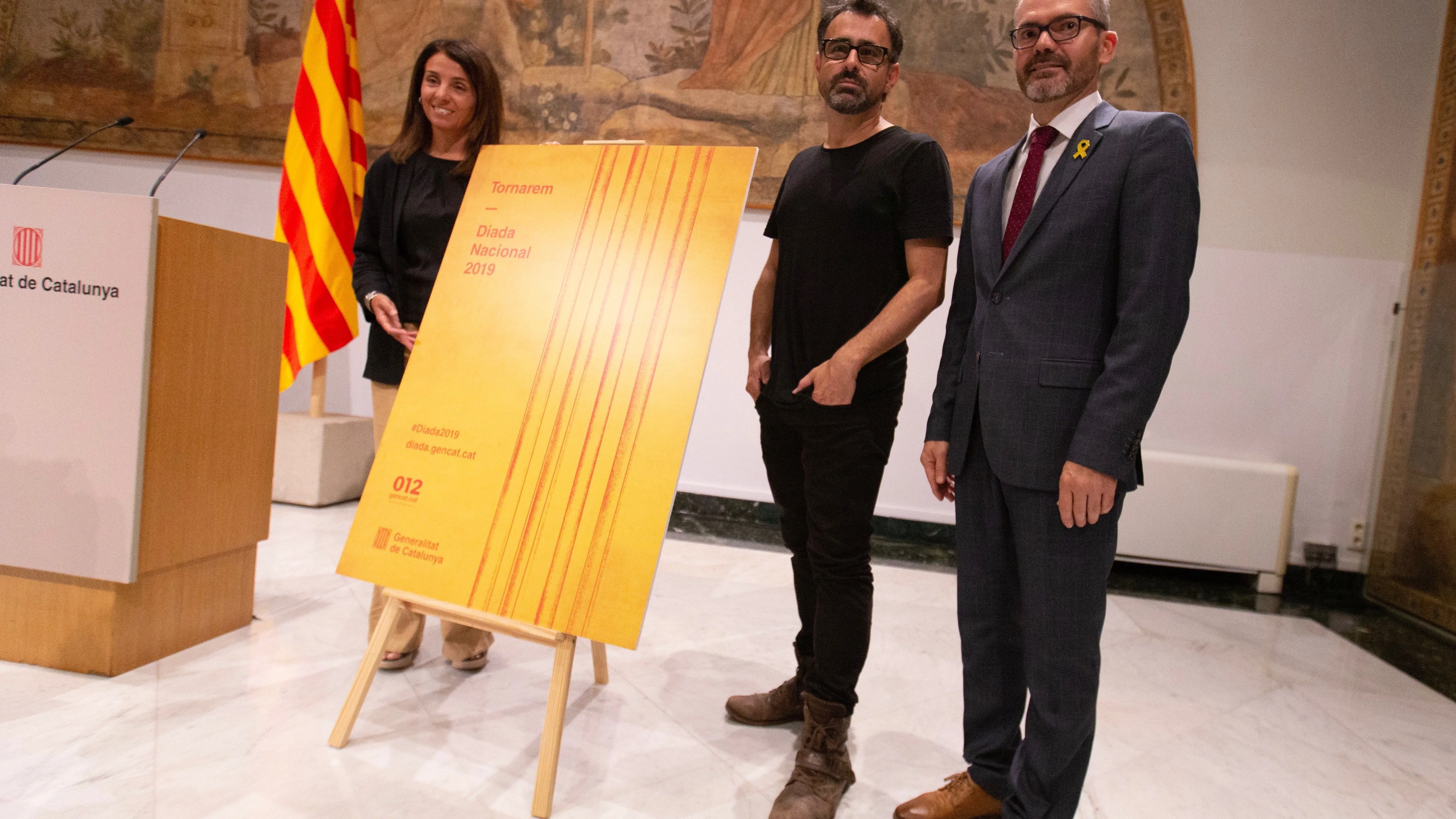 La consellera de Presidencia, Meritxell Budó, y el vicepresidente del Parlament, Josep Costa, acompañados del creador artístico del cartel del acto oficial de la Diada.