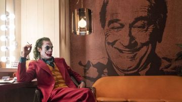 Joker (Joaquin Phoenix) con una imagen al fondo de Murray Franklin (Robert De Niro)