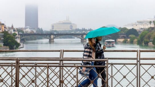Dos personas atraviesan el puente de San Telmo, con el puente de Triana y Torre Sevilla.