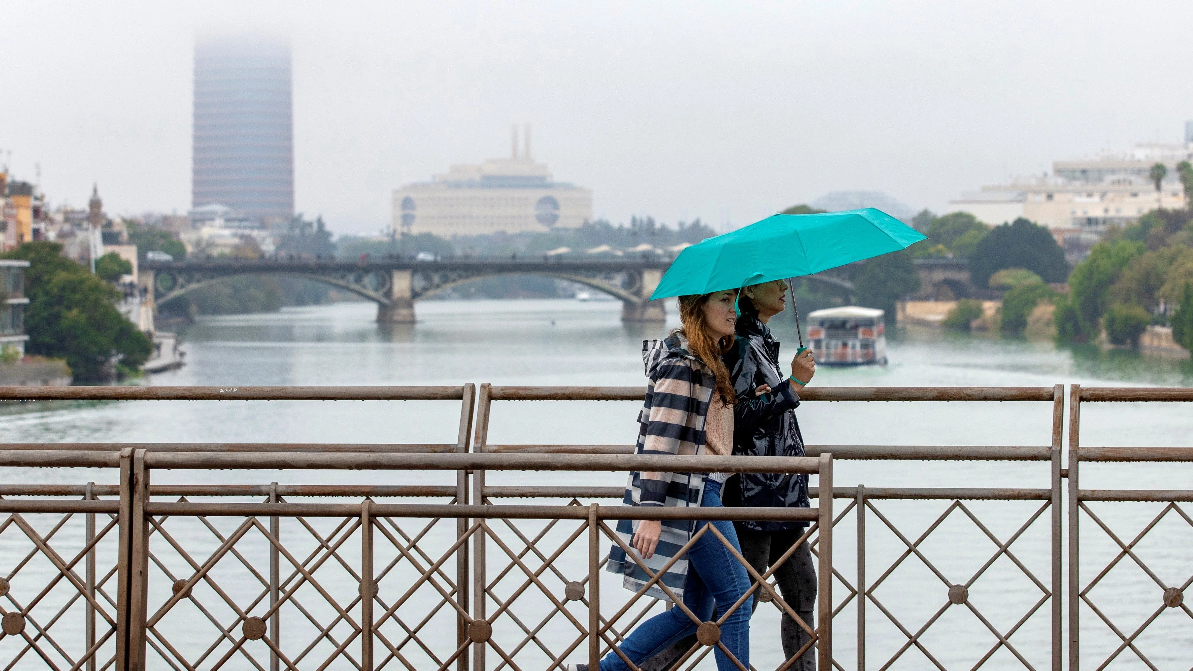 Dos personas atraviesan el puente de San Telmo, con el puente de Triana y Torre Sevilla.