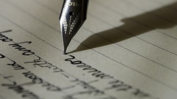Imagen de archivo de una pluma escribiendo una nota