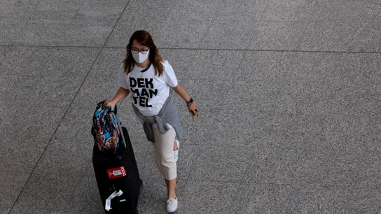 Una mujer con una mascarilla desplazándose con una maleta Una mujer con una mascarilla desplazándose con una maleta