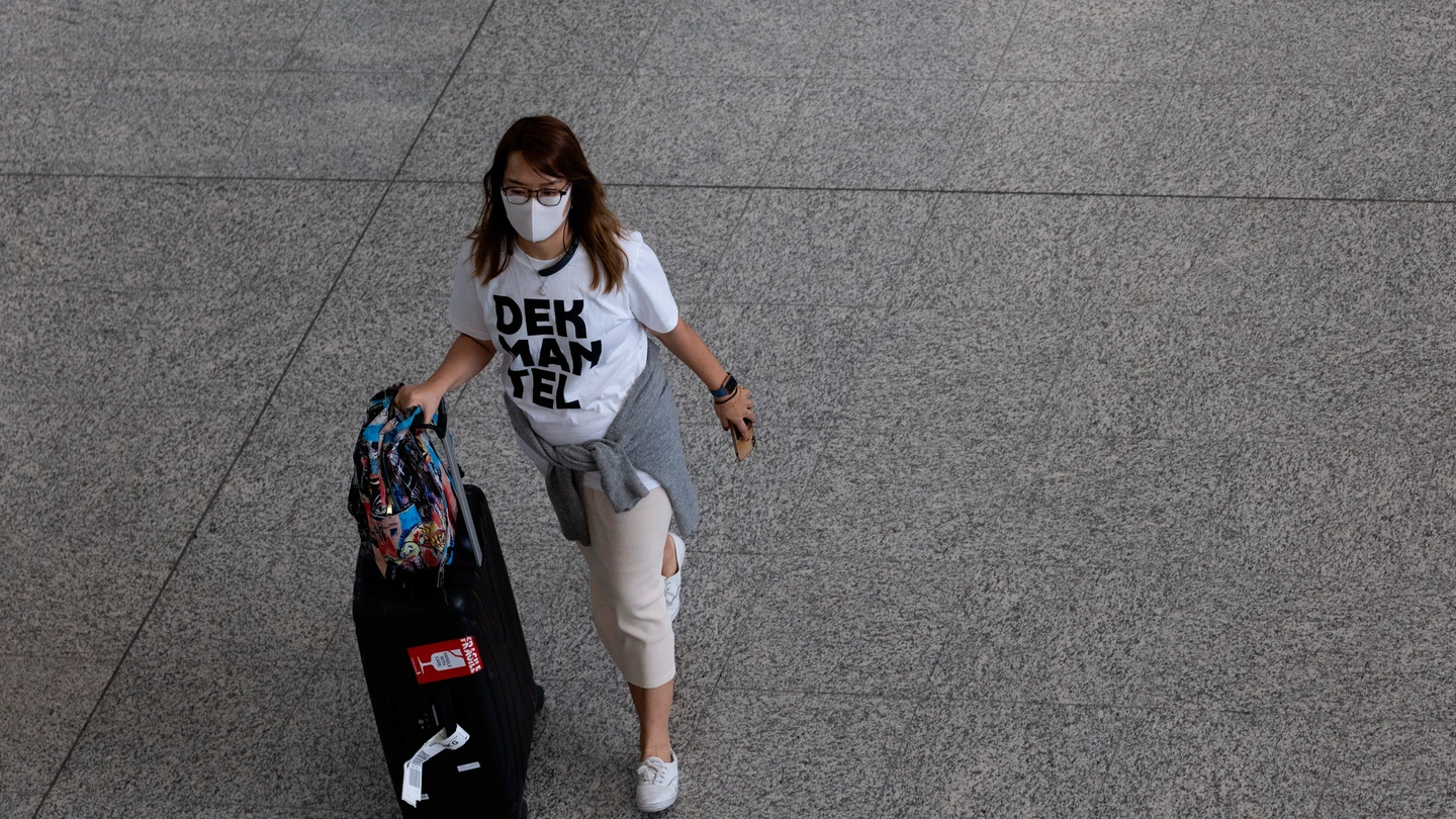 Una mujer con una mascarilla desplazándose con una maleta Una mujer con una mascarilla desplazándose con una maleta