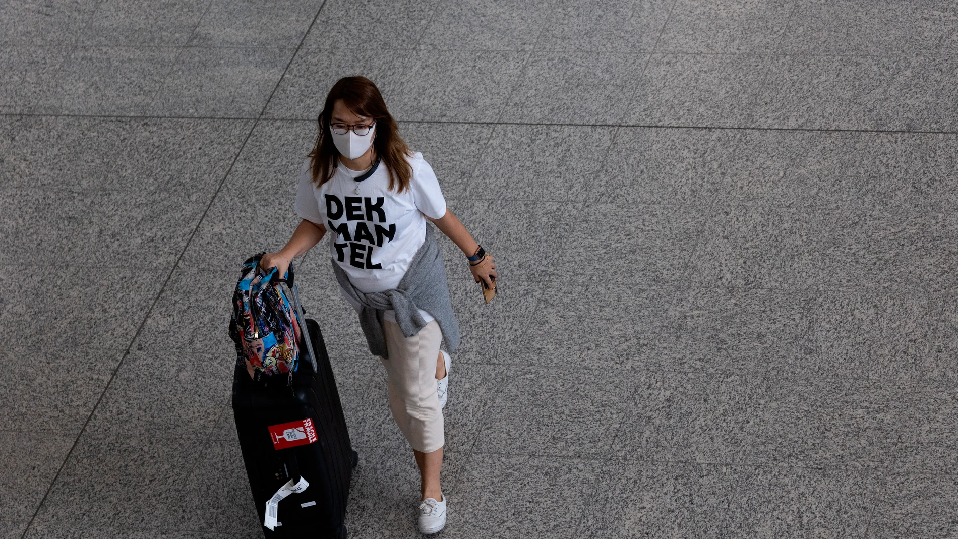 Una mujer con una mascarilla desplazándose con una maleta