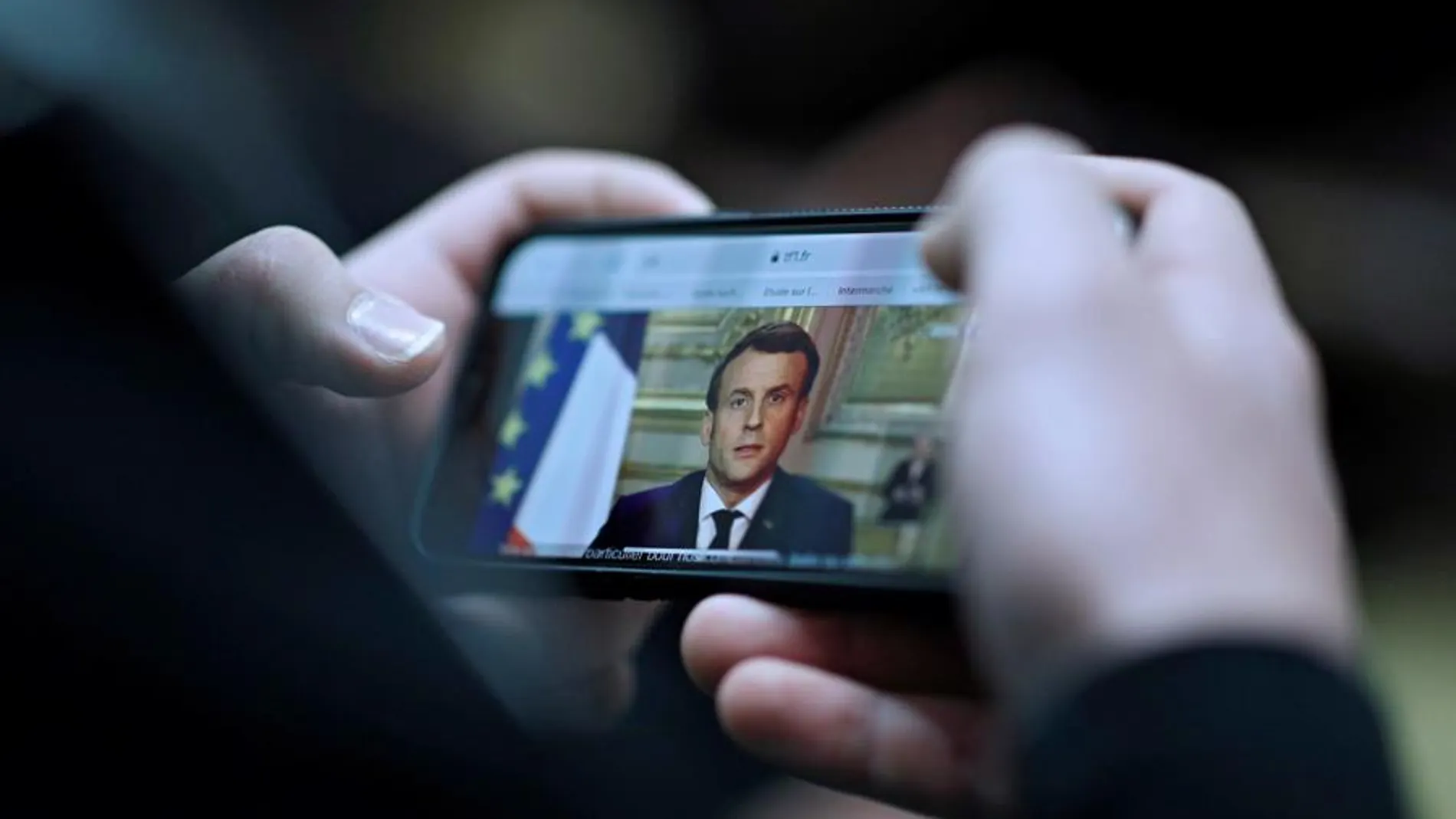 Un ciudadano sigue a través de su móvil el discurso de Emmanuel Macron