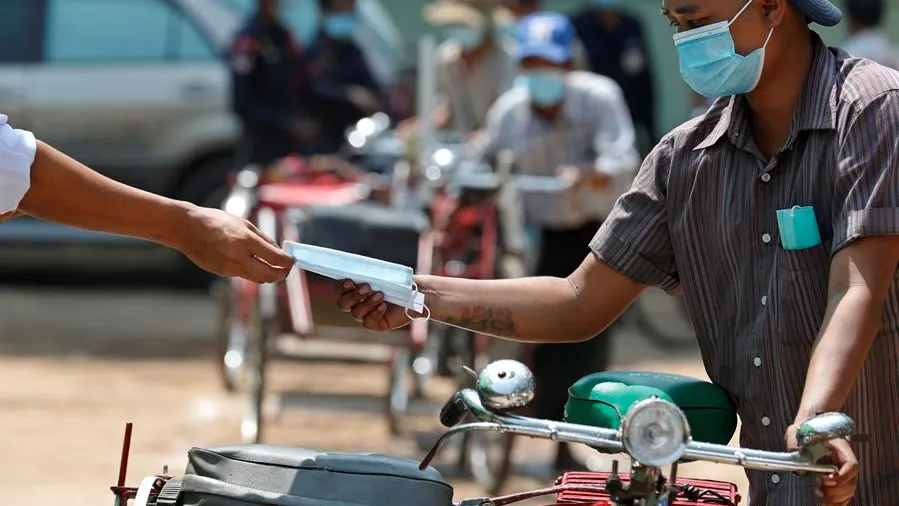 Un conductor recibe una mascarilla gratuita durante una donación de alimentos a personas con bajos ingresos en Myanmar