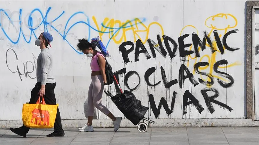 Personas con mascarilla frente a un grafitti sobre el coronavirus en Londres