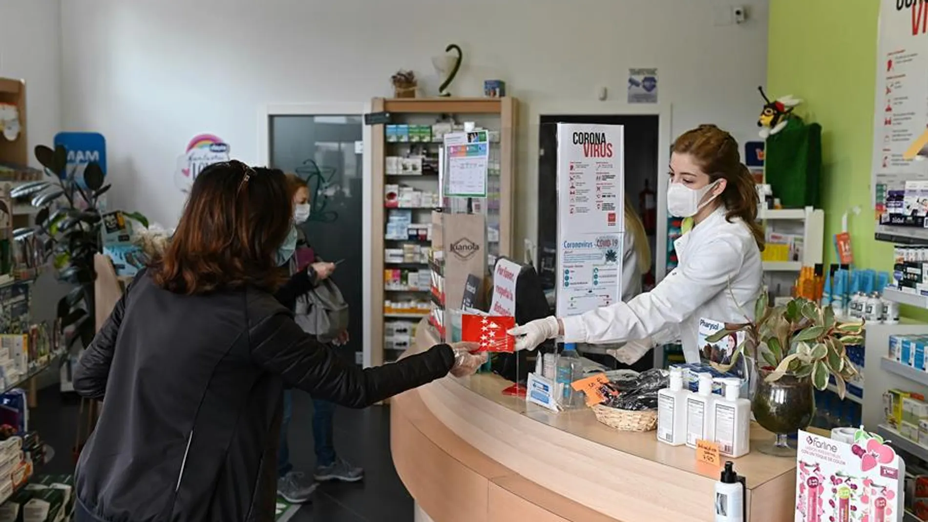 Una farmacéutica entrega una mascarilla en una farmacia madrileña