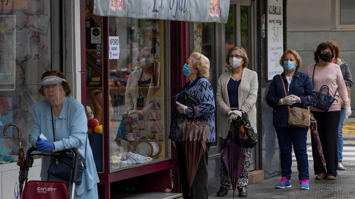 Varias mujeres con mascarillas hacen cola ante una mercería Varias mujeres con mascarillas hacen cola ante una mercería