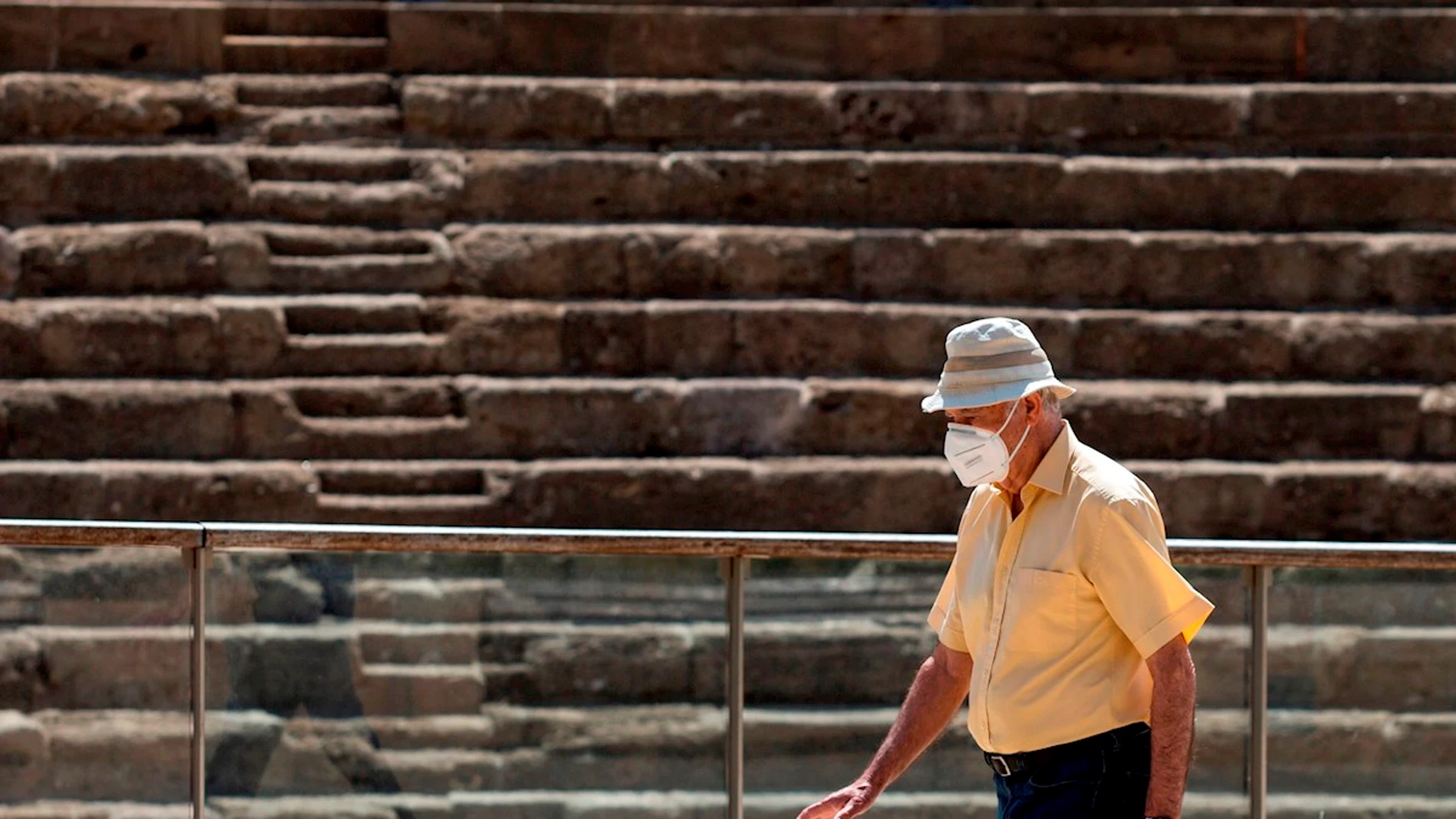 Una persona camina frente al Teatro Romano de Málaga protegiéndose con una mascarilla