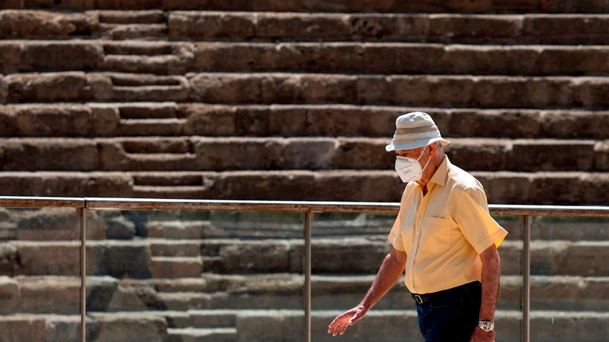 Una persona camina frente al Teatro Romano de Málaga protegiéndose con una mascarilla