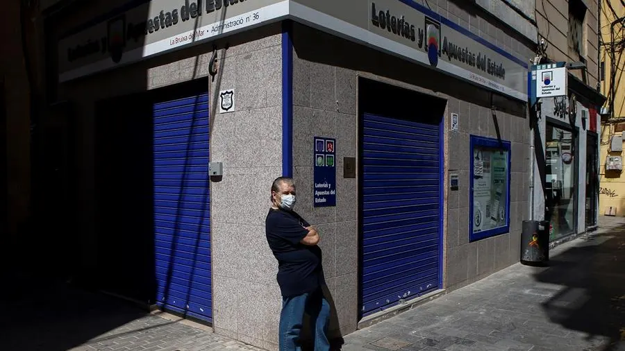 Un ciudadano con mascarilla frente a una administración de lotería en Barcelona Un ciudadano con mascarilla frente a una administración de lotería en Barcelona