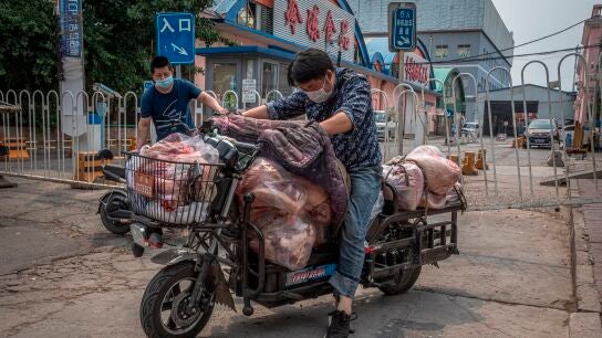 Un hombre con mascarilla montado en su moto en Pek&iacute;n, China