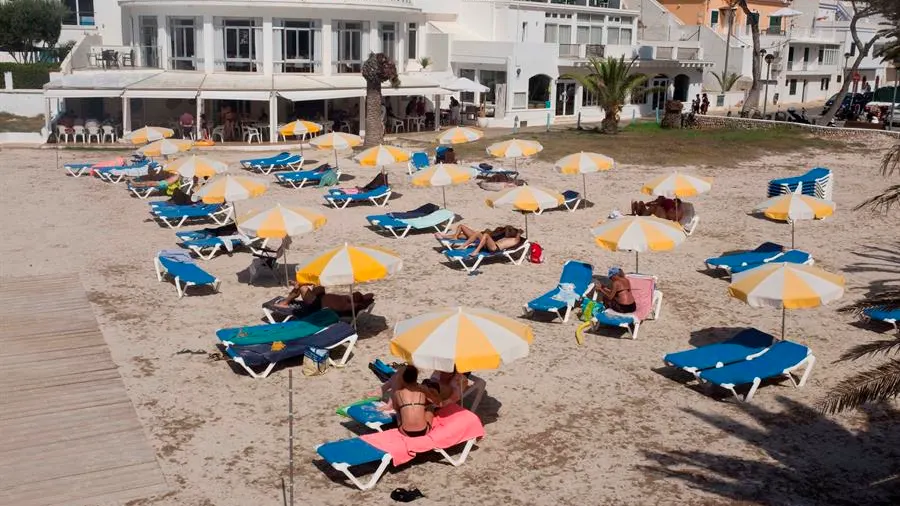 Varias personas toman el sol en la Cala Santandría de Menorca. 