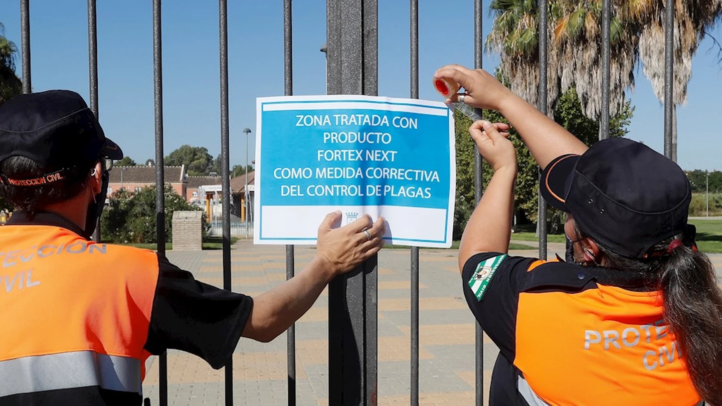 Dos miembros de protección civil colocan un cartel tras la fumigación de uno de los jardines de Coría del Río Dos miembros de protección civil colocan un cartel tras la fumigación de uno de los jardines de Coría del Río