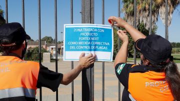 Dos miembros de protección civil colocan un cartel tras la fumigación de uno de los jardines de Coría del Río