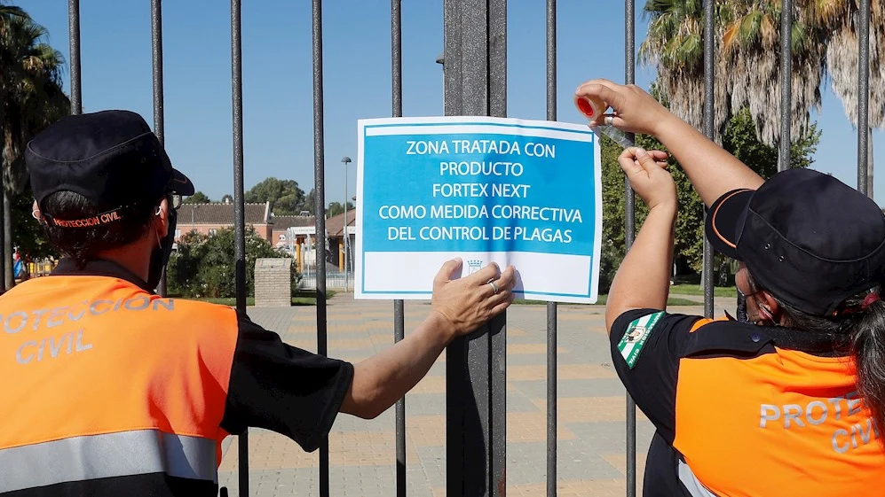 Dos miembros de protección civil colocan un cartel tras la fumigación de uno de los jardines de Coría del Río