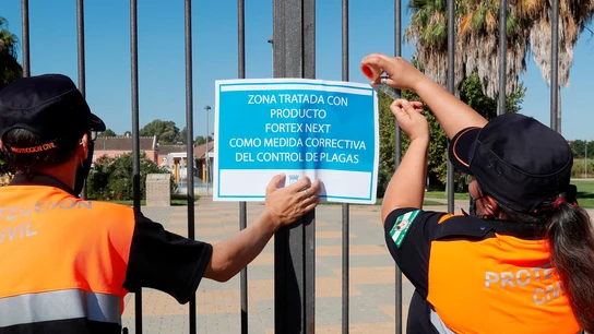 Dos miembros de protección civil colocan un cartel tras la fumigación de uno de los jardines de Coría del Río Dos miembros de protección civil colocan un cartel tras la fumigación de uno de los jardines de Coría del Río