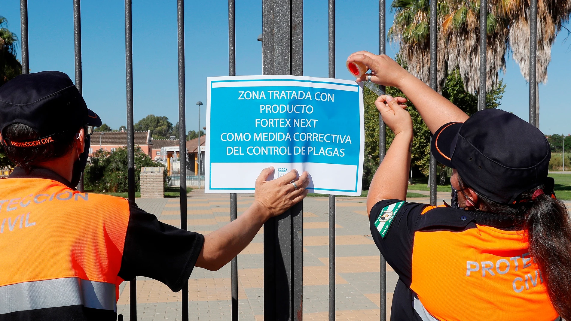 Dos miembros de protección civil colocan un cartel tras la fumigación de uno de los jardines de Coría del Río