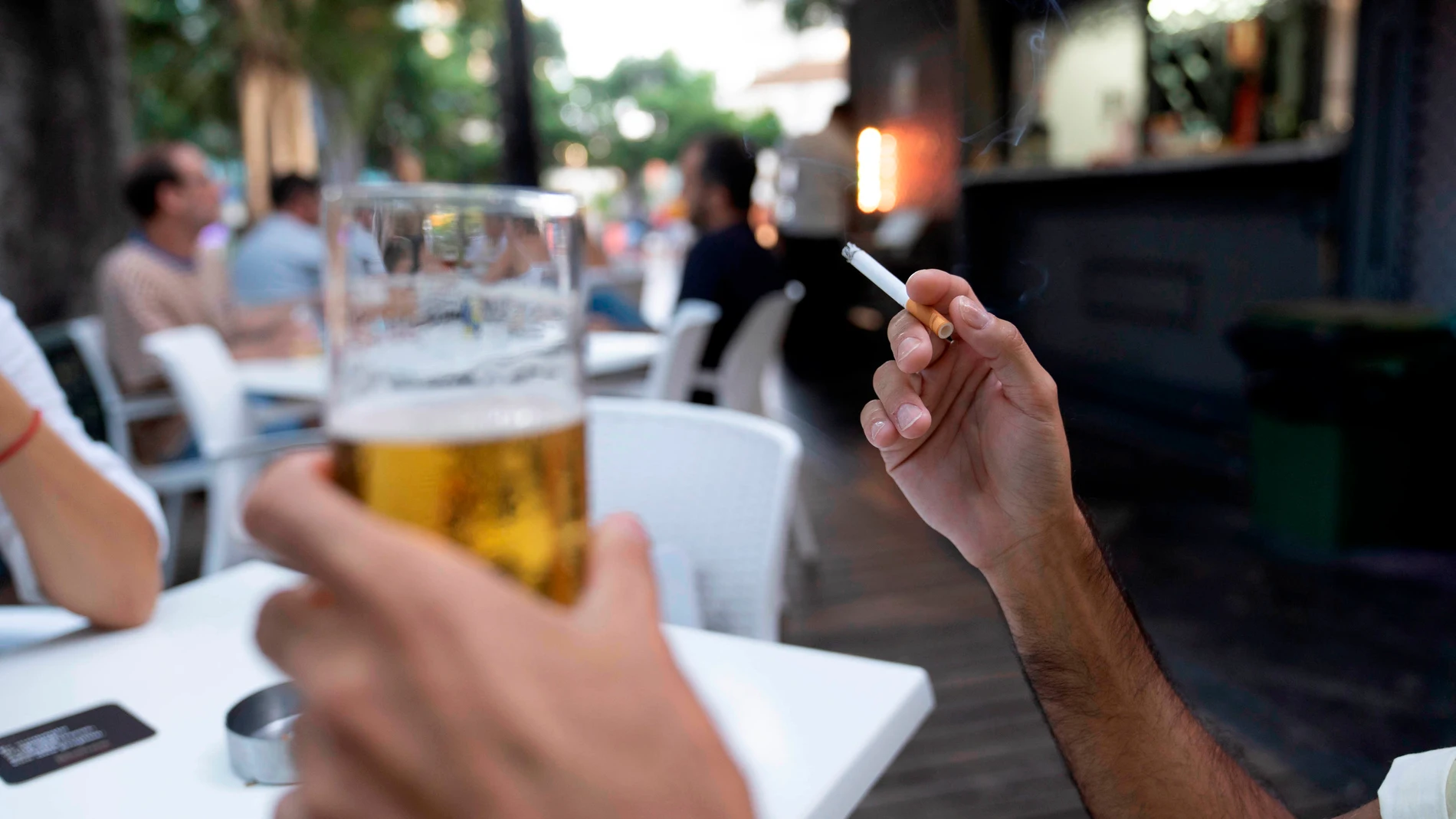 Una persona sostiene un cigarrillo en la terraza de en un bar