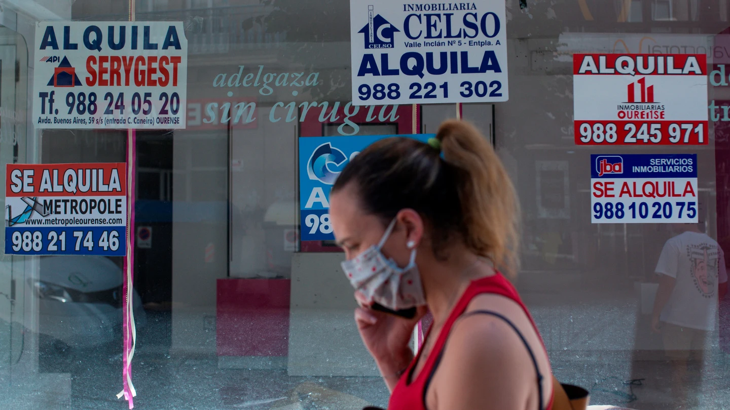 Una mujer con mascarilla pasa ante un comercio cerrado con varios carteles que anuncian su alquiler Una mujer con mascarilla pasa ante un comercio cerrado con varios carteles que anuncian su alquiler