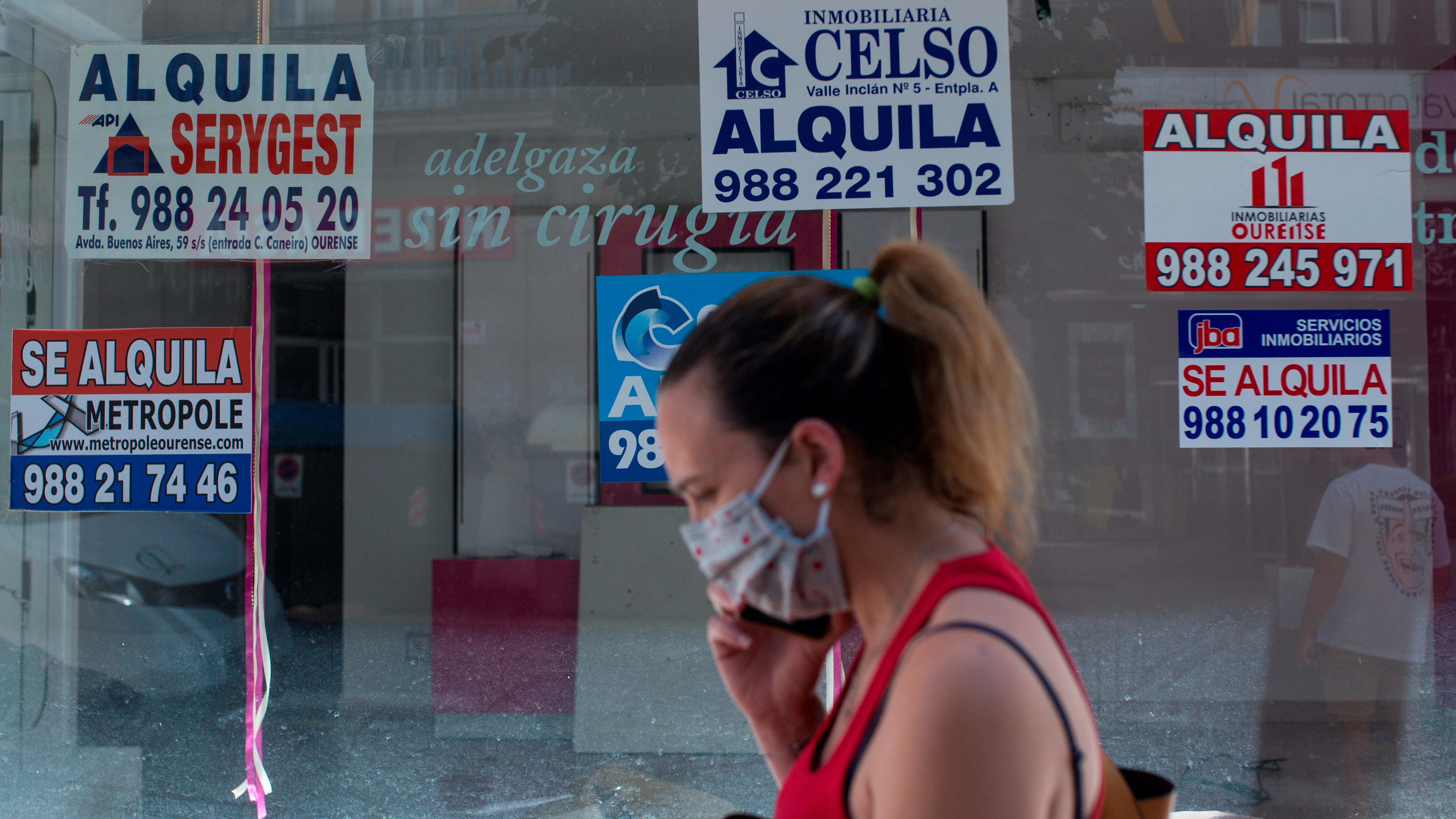 Una mujer con mascarilla pasa ante un comercio cerrado con varios carteles que anuncian su alquiler