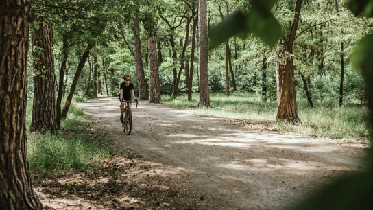 Una mujer hace deporte en bicicleta por un camino en medio de la naturaleza Una mujer hace deporte en bicicleta por un camino en medio de la naturaleza