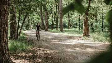 Una mujer hace deporte en bicicleta por un camino en medio de la naturaleza