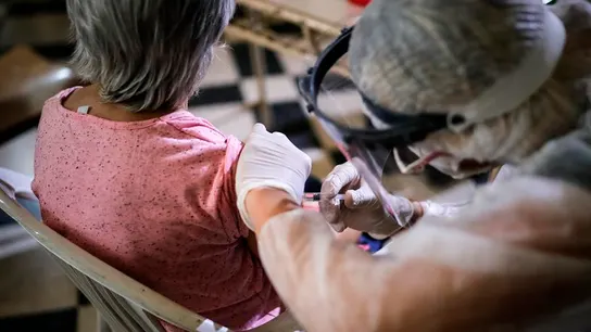 Una enfermera con EPI vacuna a una mujer de la gripe Una enfermera con EPI vacuna a una mujer de la gripe
