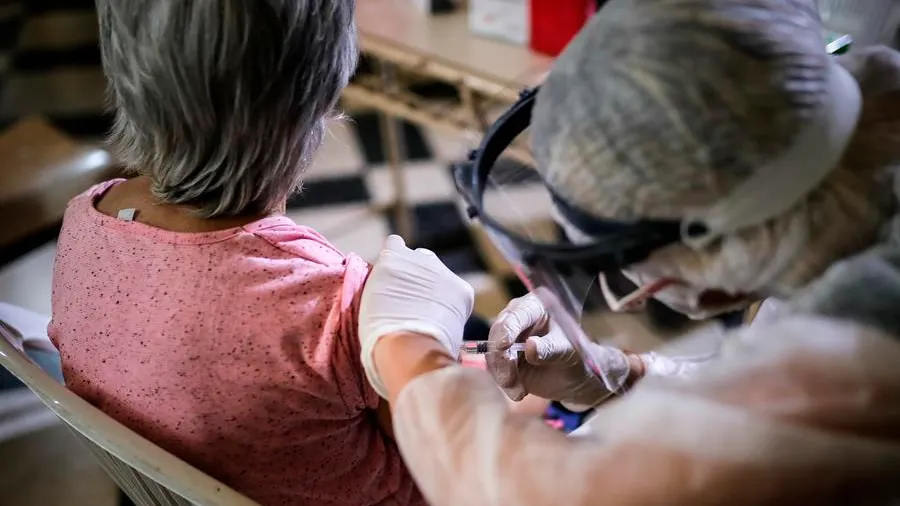 Una enfermera con EPI vacuna a una mujer de la gripe