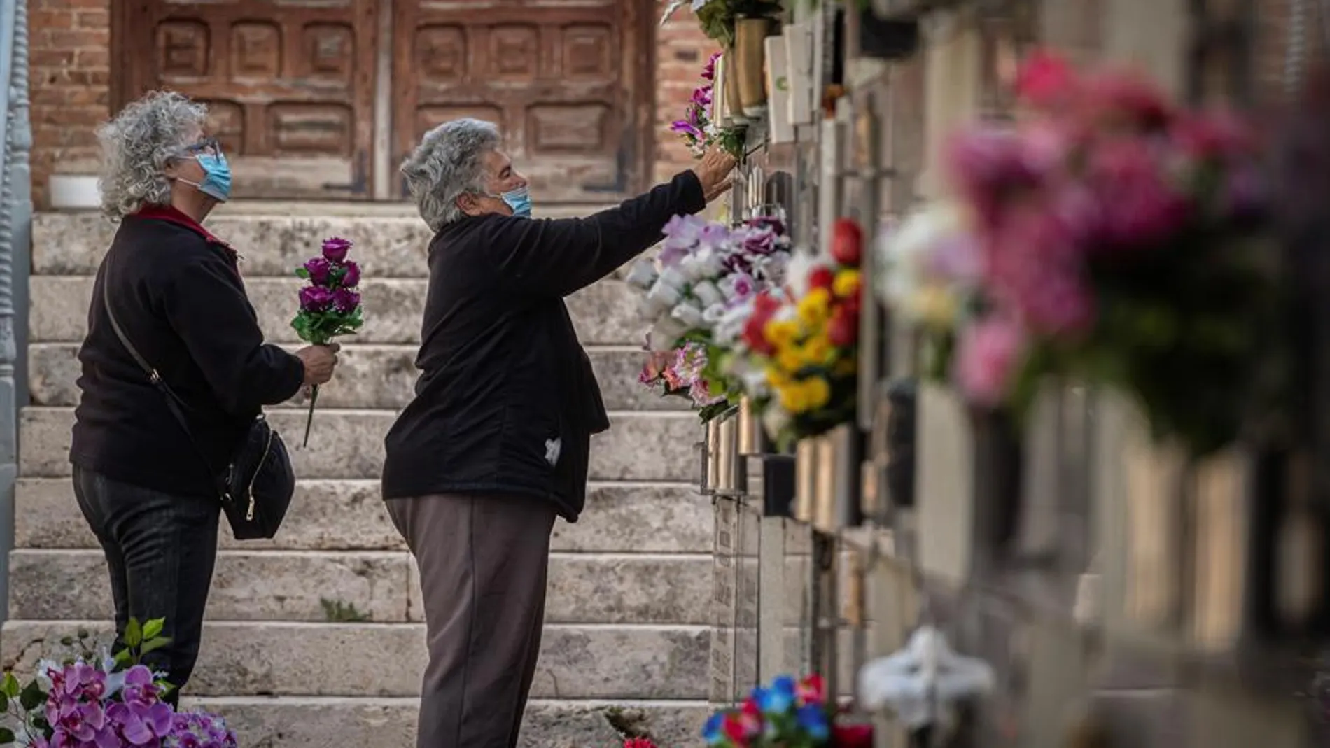 Varias mujeres colocan flores en una tumba del cementerio de Alcalá