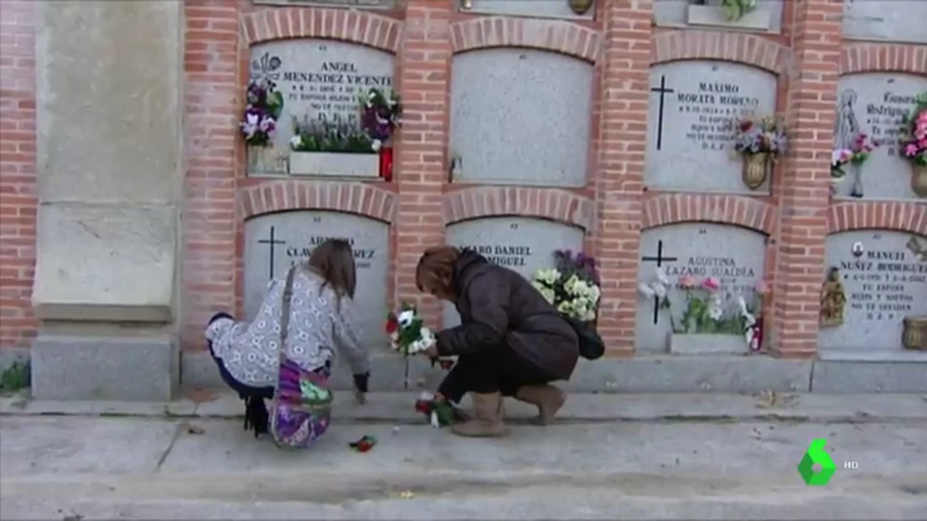 Dos mujeres dejan flores en un cementerio