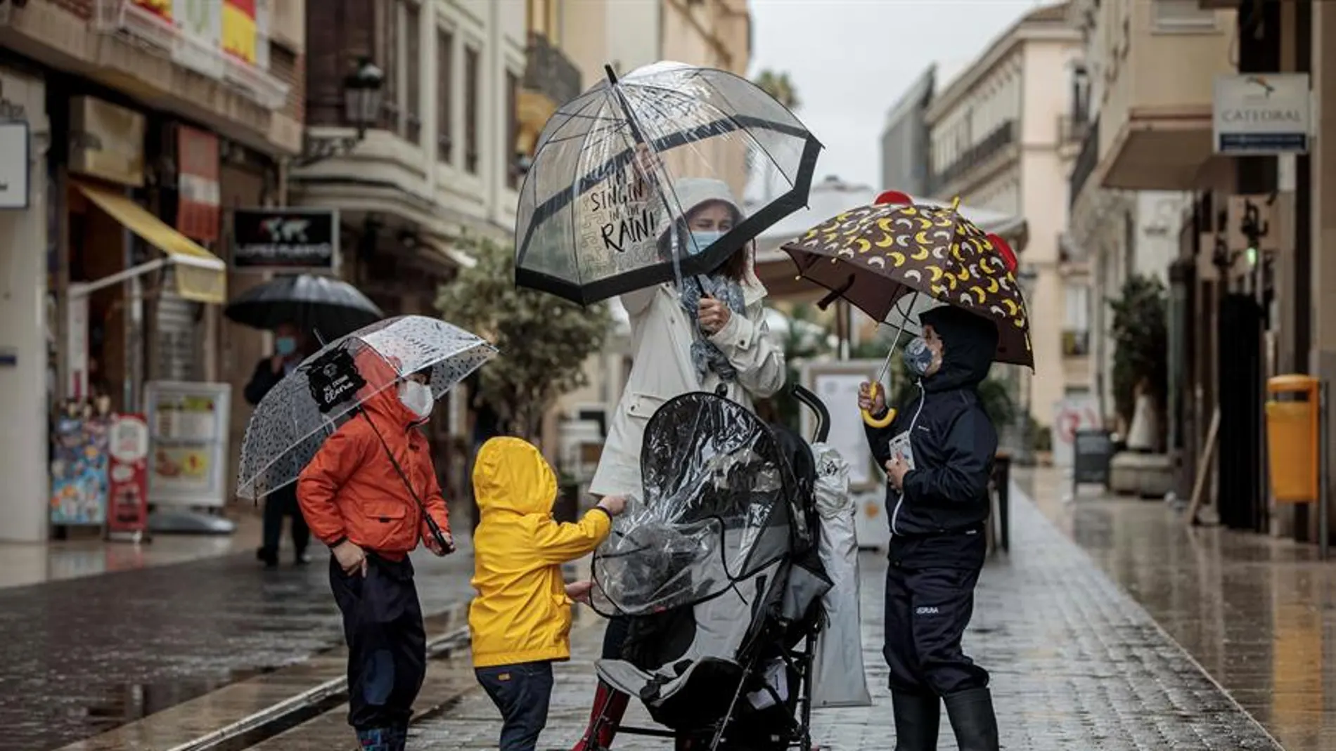 Una mujer con tres menores se protegen de la lluvia con paraguas y chubasqueros