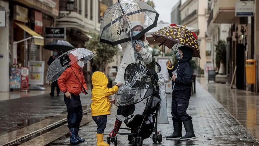 Una mujer con tres menores se protegen de la lluvia con paraguas y chubasqueros