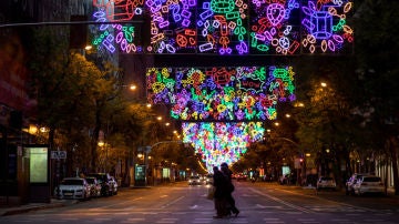 Varias personas cruzan por un paso de cebra de la calle Goya, en Madrid, bajo una colorida iluminación de Navidad
