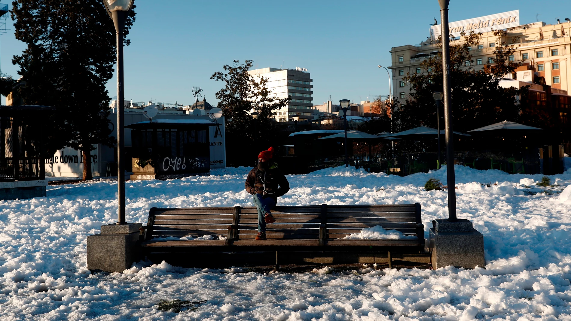 Un hombre sentado en un banco, rodeado de nieve este lunes en la plaza de Colón de Madrid