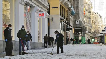 Varias personas limpian la nieve y el hielo de las aceras en la Gran Vía de Madrid
