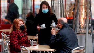 Una camarera sirve a dos clientes en una terraza de Valencia.