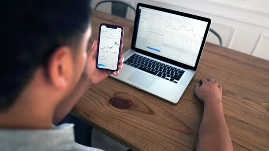 Un hombre realiza unas gestiones con su ordenador y su teléfono móvil ¿Cómo tributan los dividendos y los fondos de inversión en la declaración de la renta 2020/21?