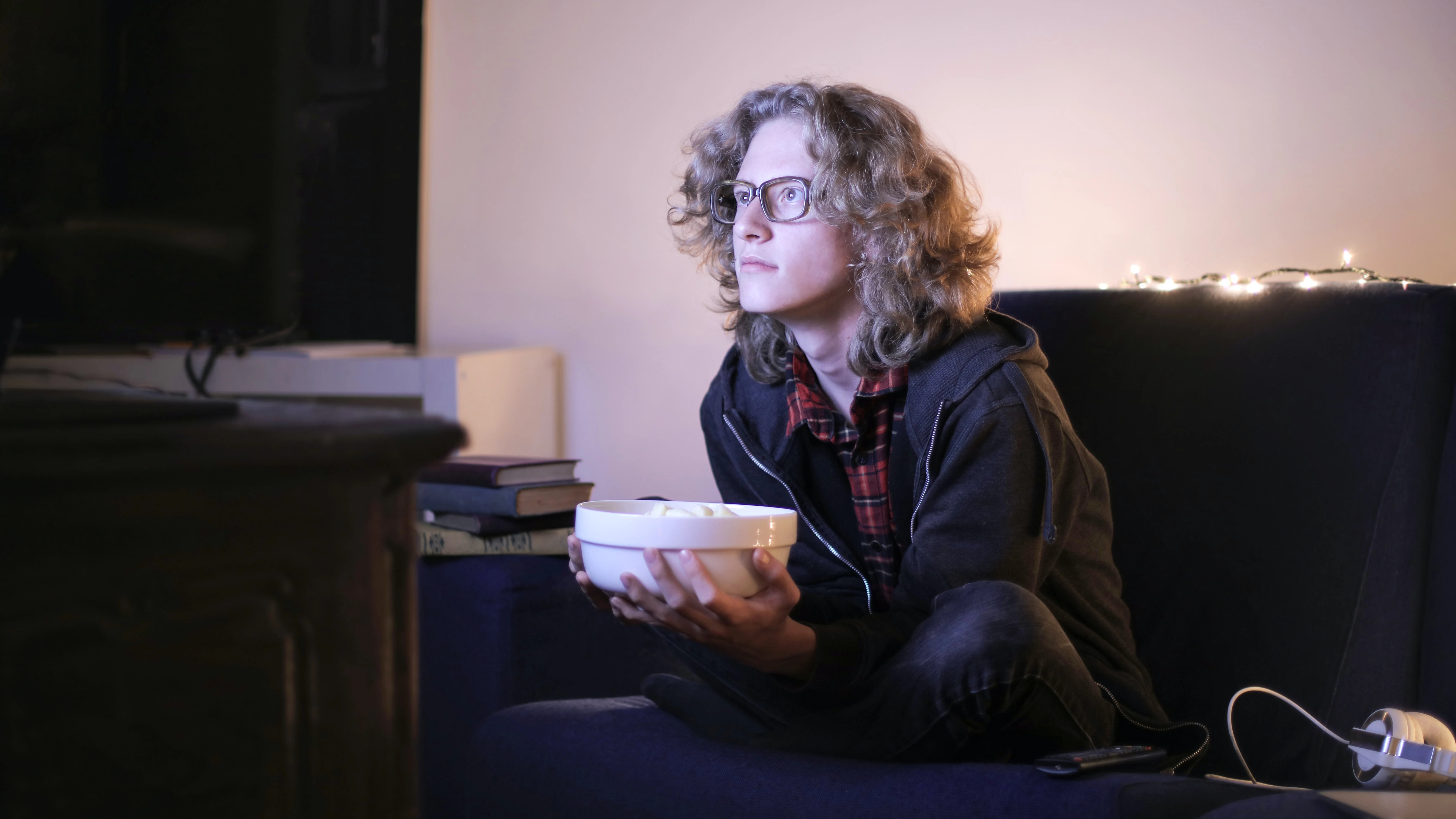 Una chica está sentada en el sofá viendo la televisión y comiendo palomitas