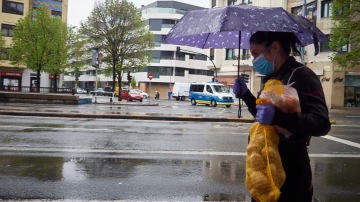 Una mujer se protege de la lluvia con un paraguas mientras camina con una bolsa de patatas durante el Martes Santo